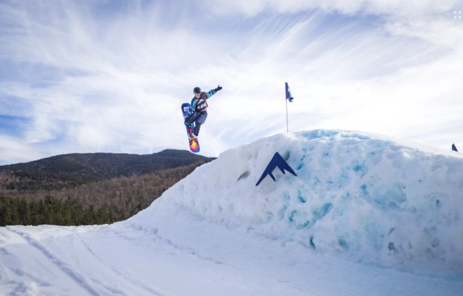 Snowboarder jumps off of large snow jump with Whiteface logo superimposed on snow
